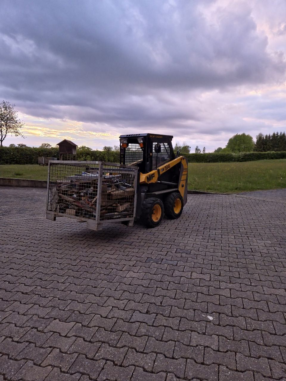 Entrümpelung: Kompaktlader transportiert eine Gitterbox mit Altholz